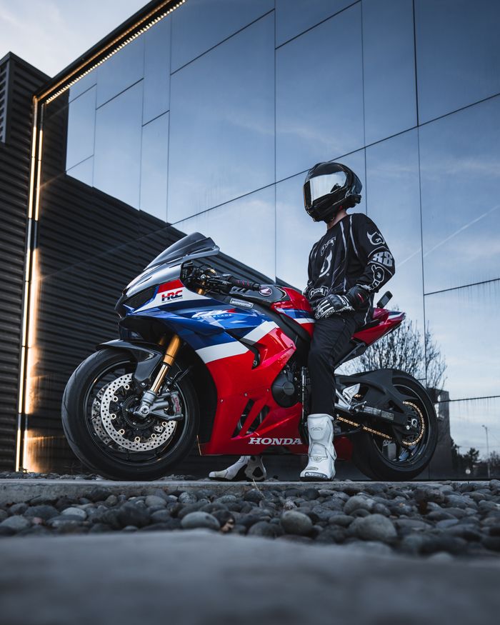 Biker in gear with helmet and vibrant sport motorcycle near modern building.